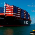 Un buque carguero estadounidense con contenedores estampados con su bandera se aproxima a Colombia, mientras una lancha colombiana con pocos contenedores se aleja, simbolizando el déficit comercial tras trece años del TLC entre Colombia y EE. UU.