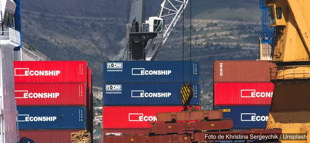 Grúa portuaria mueve contenedores rojos y azules en terminal marítimo de comercio internacional colombiano