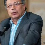 Gustavo Petro hablando frente a micrófono con la bandera de Colombia al fondo durante discurso oficial