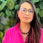 María Alejandra Osorio posa con camisa fucsia frente a un muro cubierto de hojas verdes